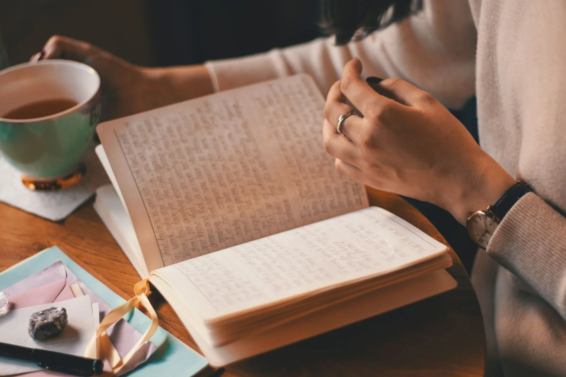 Hands writing in an open notebook next to a cup of tea